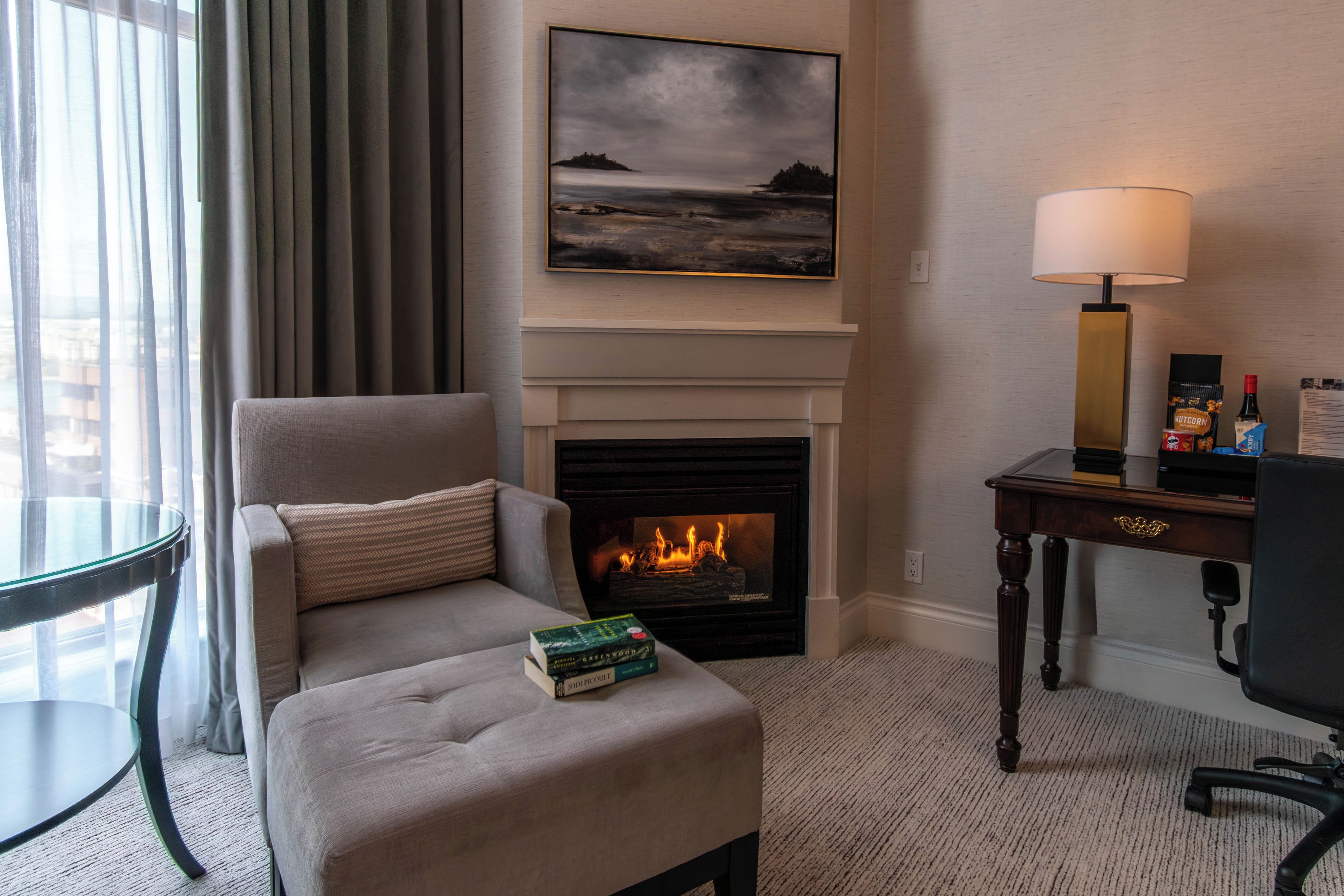 A hotel room with a fireplace, a sofa, a table, and a lamp.
