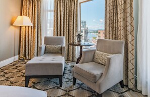 A hotel room with two armchairs, a small table with a bottle and glasses, and a view of a cityscape through large windows. - The Magnolia Hotel and Spa (Victoria)