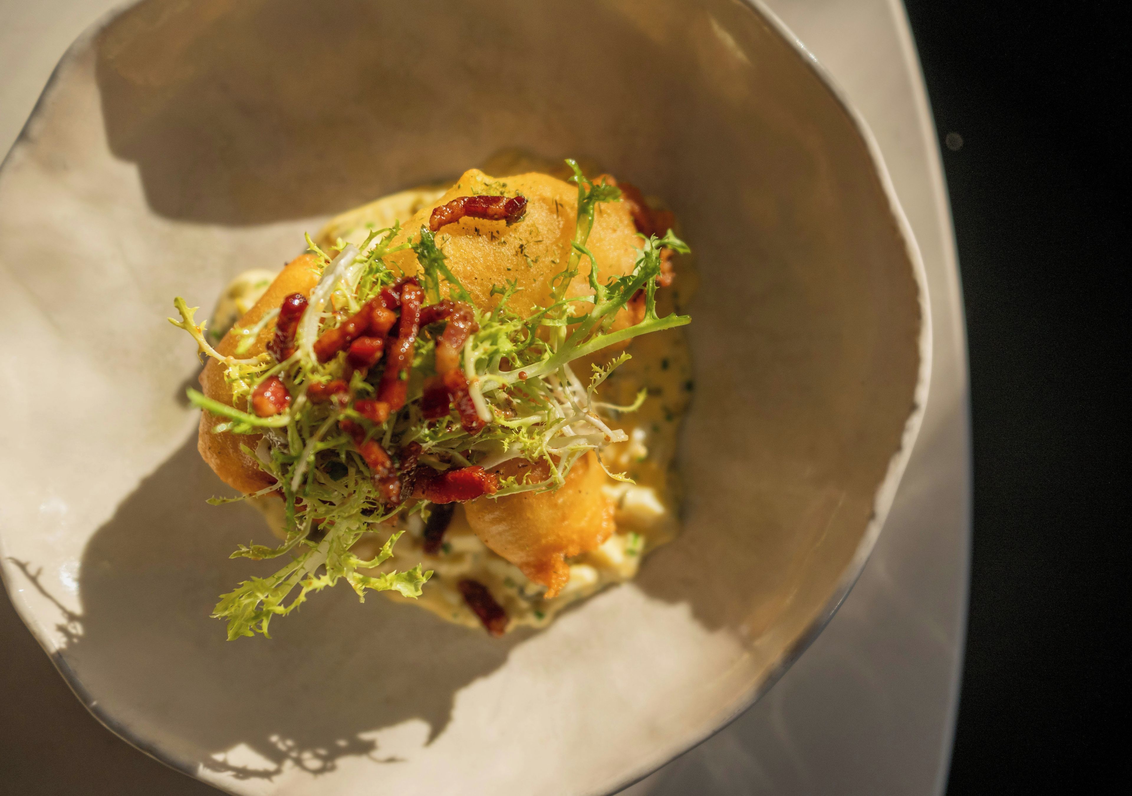 A bowl containing a food item with greens and a crispy element.