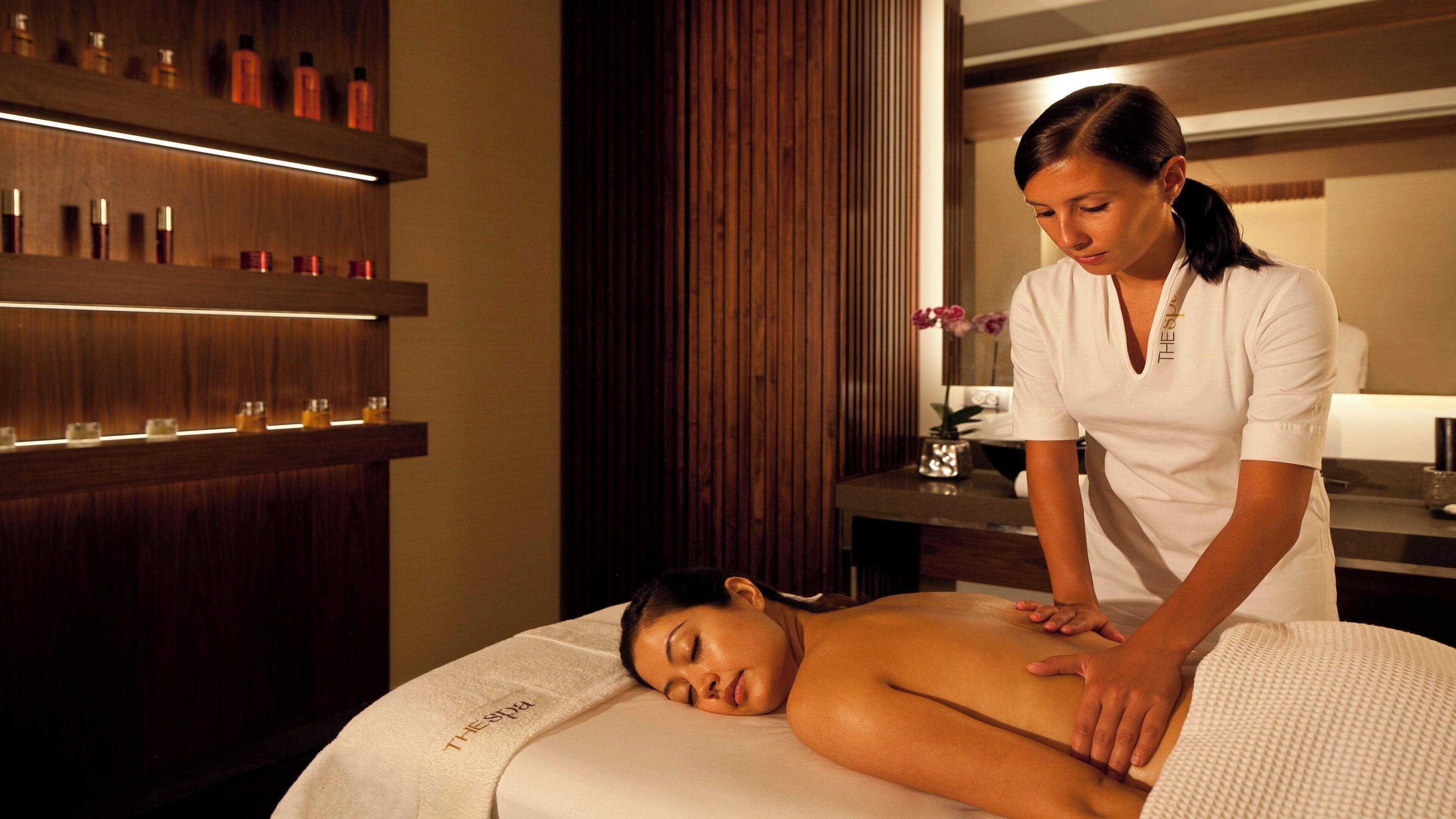 Un espace de spa comprenant une table de massage, une personne recevant un massage et des étagères remplies de bouteilles.