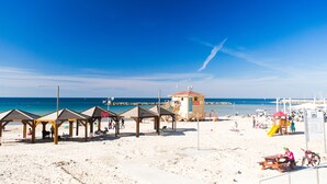 Une plage avec des pergolas en bois, un poste de surveillance pour les sauveteurs et une aire de jeux.
