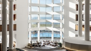 Un hall d’hôtel moderne avec vue sur la piscine, comprenant un espace salon central et de grandes fenêtres.