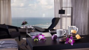 Une chambre d’hôtel avec vue sur l’océan, une table à manger avec des pâtisseries et une tasse de café, et une chaise.