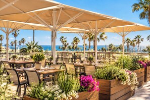 An outdoor dining area with tables and chairs, umbrellas, and potted plants.