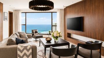Una habitación de hotel moderna con una amplia vista al océano, un televisor de pantalla plana en la pared, un sofá, una mesa de centro y una zona de comedor.