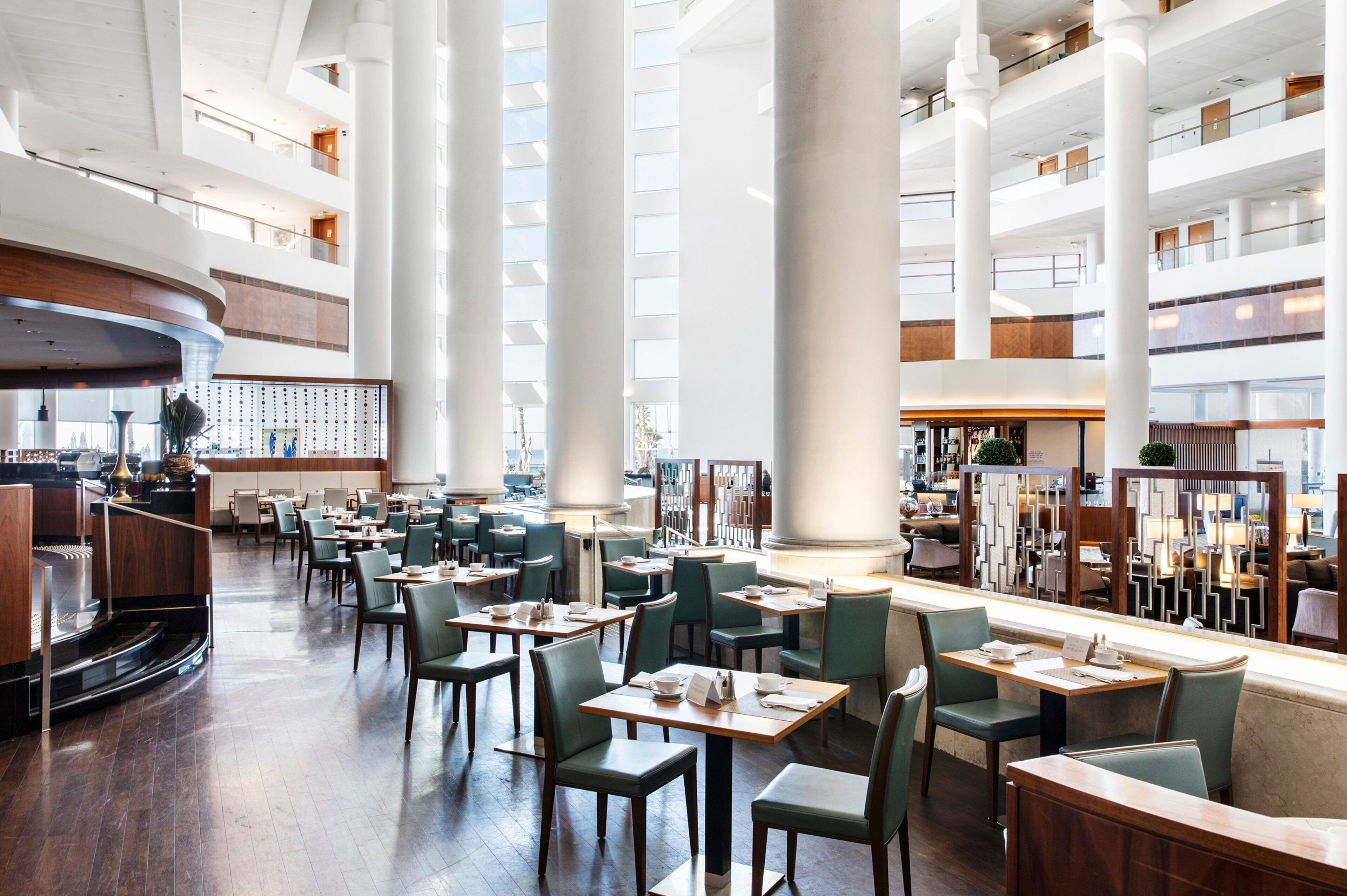 A spacious hotel lobby with multiple dining areas, high ceilings, and large windows.