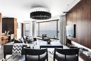 A modern living room with a large window, a sofa, a dining table, and a TV mounted on the wall.
