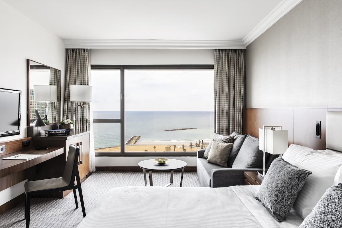 Una habitación de hotel con una ventana grande, un escritorio, una silla, una cama y una mesita.