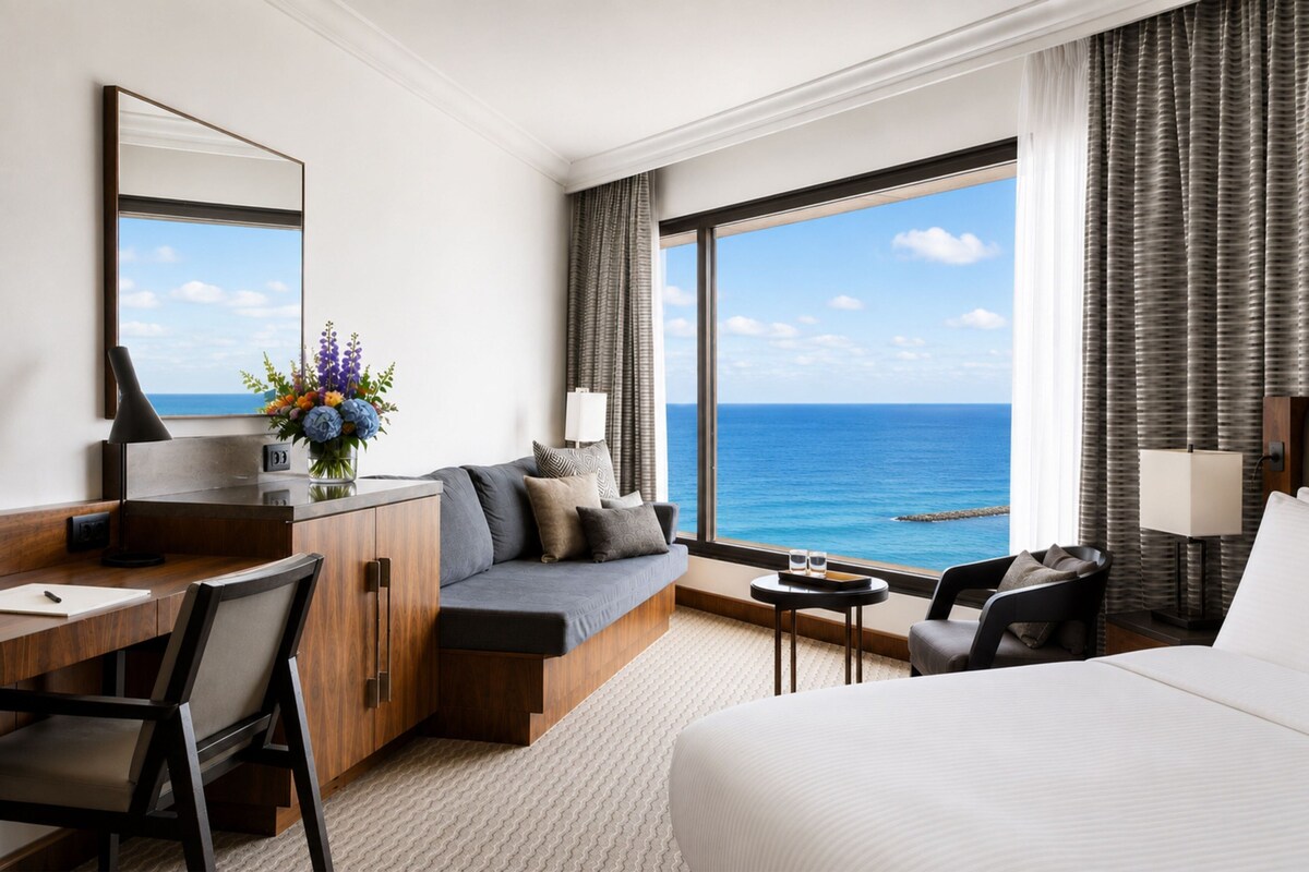 A hotel room with a bed, a desk, a sofa, and a view of the ocean.