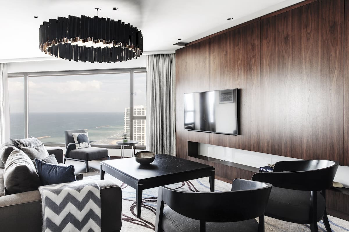 Una habitación de hotel moderna con un ventanal grande, un televisor de pantalla plana, un sofá, una mesa de comedor y una araña.