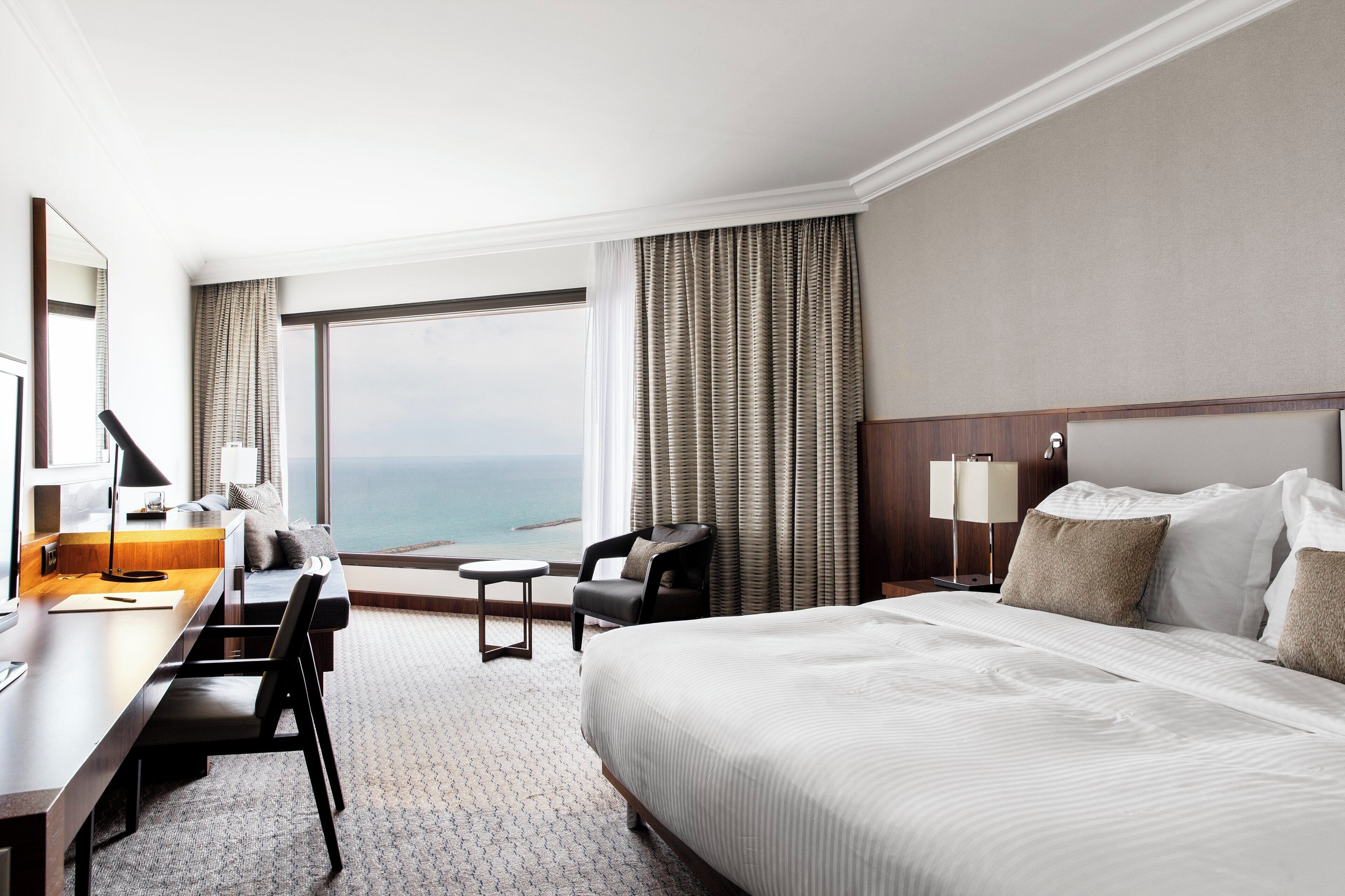 A hotel room with a large bed, a desk, a chair, and a view of the ocean.