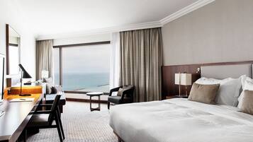 A hotel room with a large bed, a desk, a chair, and a view of the ocean.