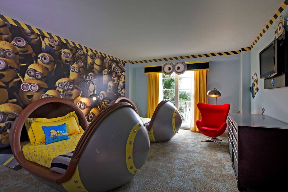 Une pièce avec un mur décoré sur le thème des Minions, une chaise rouge et un bureau avec des tiroirs.