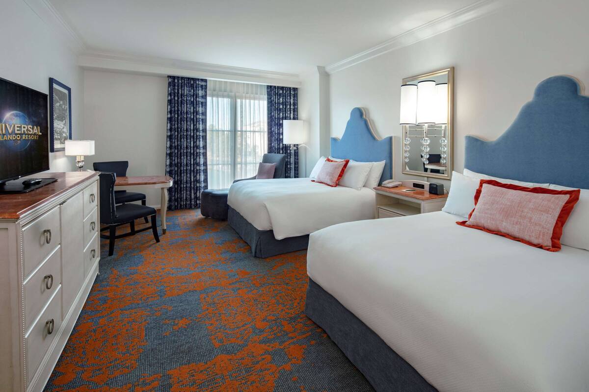 Une chambre d’hôtel avec deux lits, un bureau, une chaise, une commode et un grand miroir.