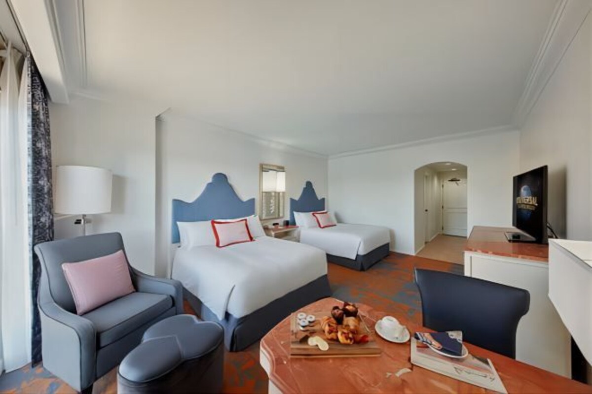 Een hotelkamer met twee bedden, een bank, een eettafel met eten en een televisie.