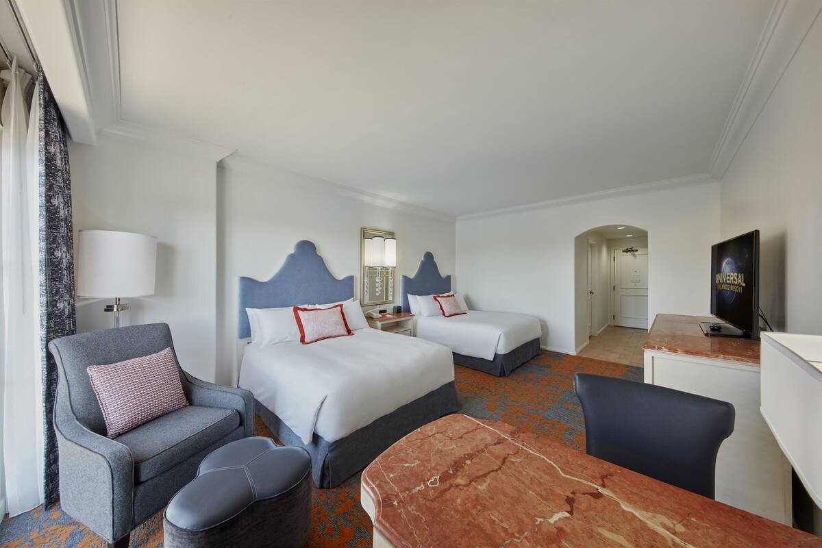 Une chambre d’hôtel avec deux lits, un bureau, une chaise, un canapé et une télévision.