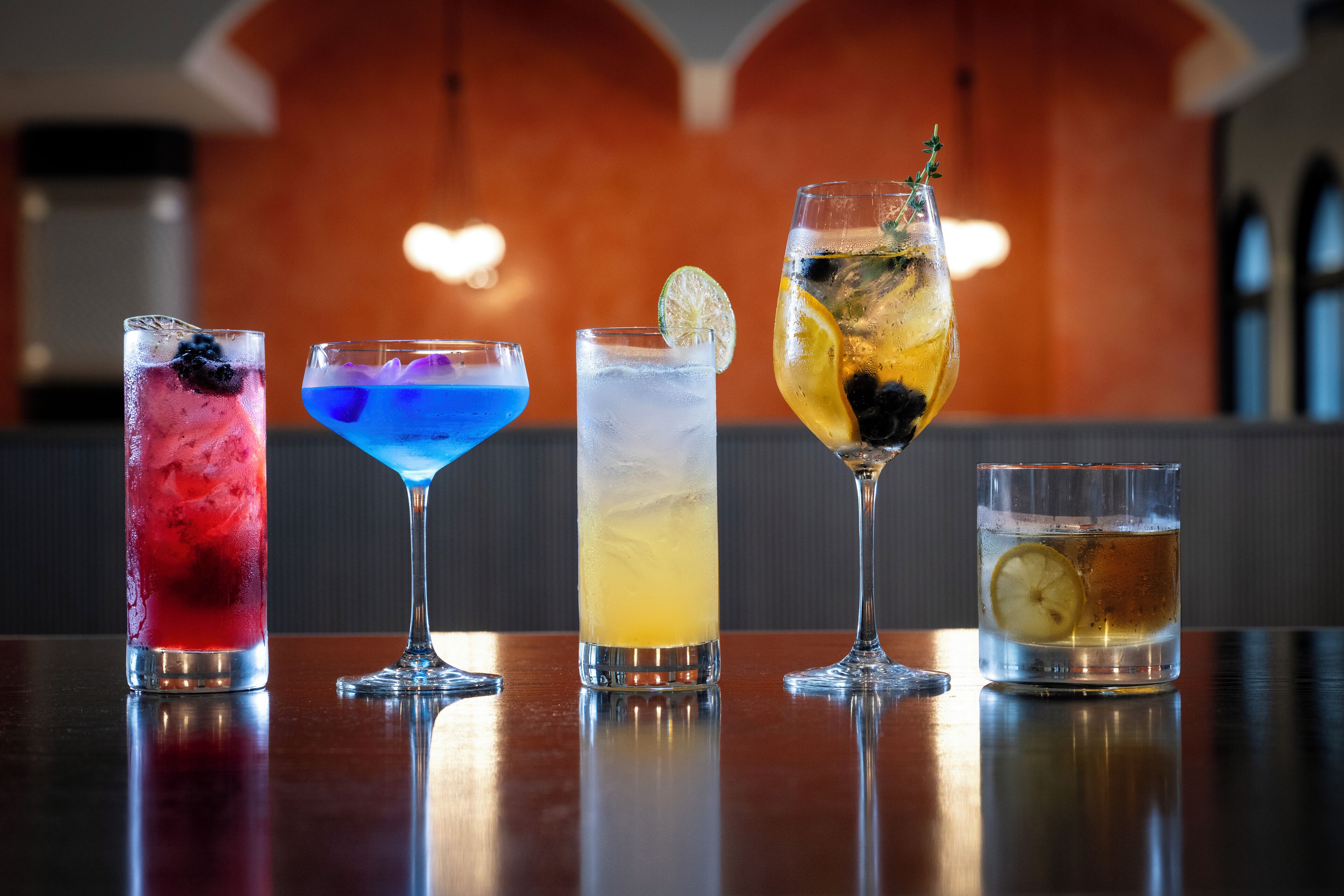 Four different cocktails on a bar counter with a warm-toned background.