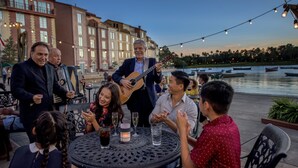 A group of people seated around a table outdoors, with a musician playing a guitar. - Universal’s Loews Portofino Bay Hotel (Orlando)