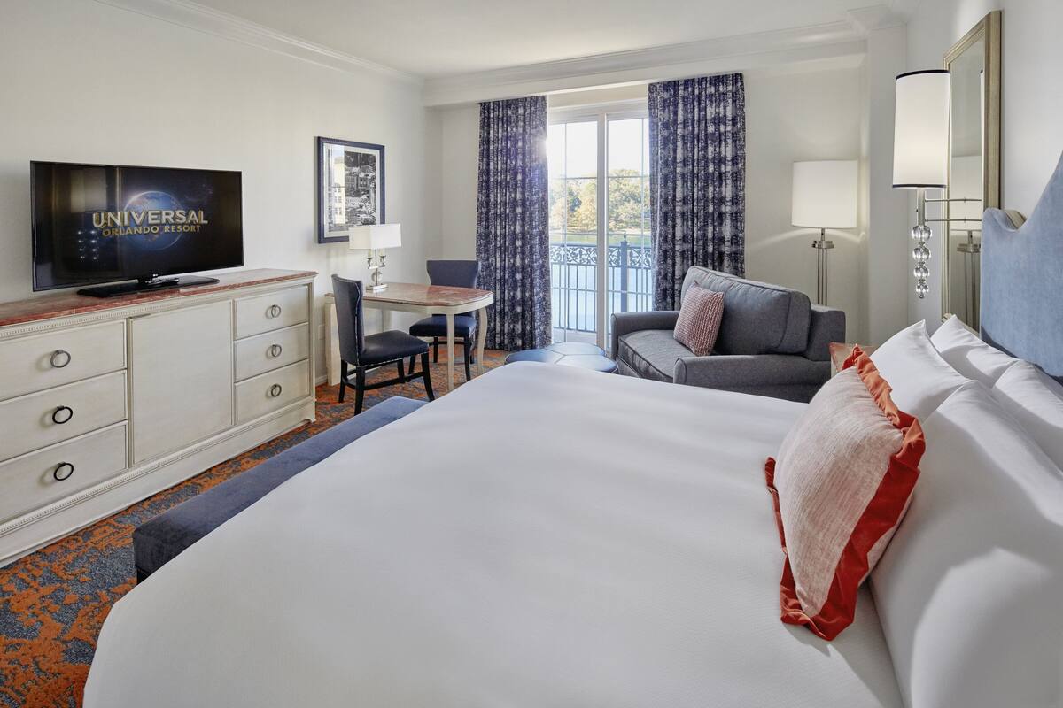 Une chambre d’hôtel avec un grand lit, un bureau avec une télévision, une chaise, un canapé et un balcon avec des rideaux.