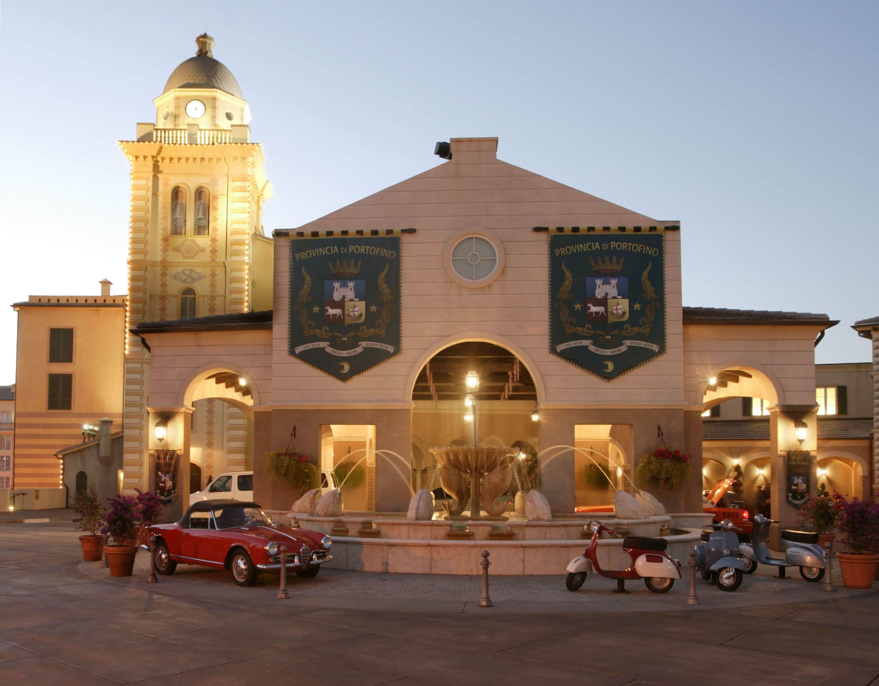 A building with two banners, a fountain, and a clock tower in the background.