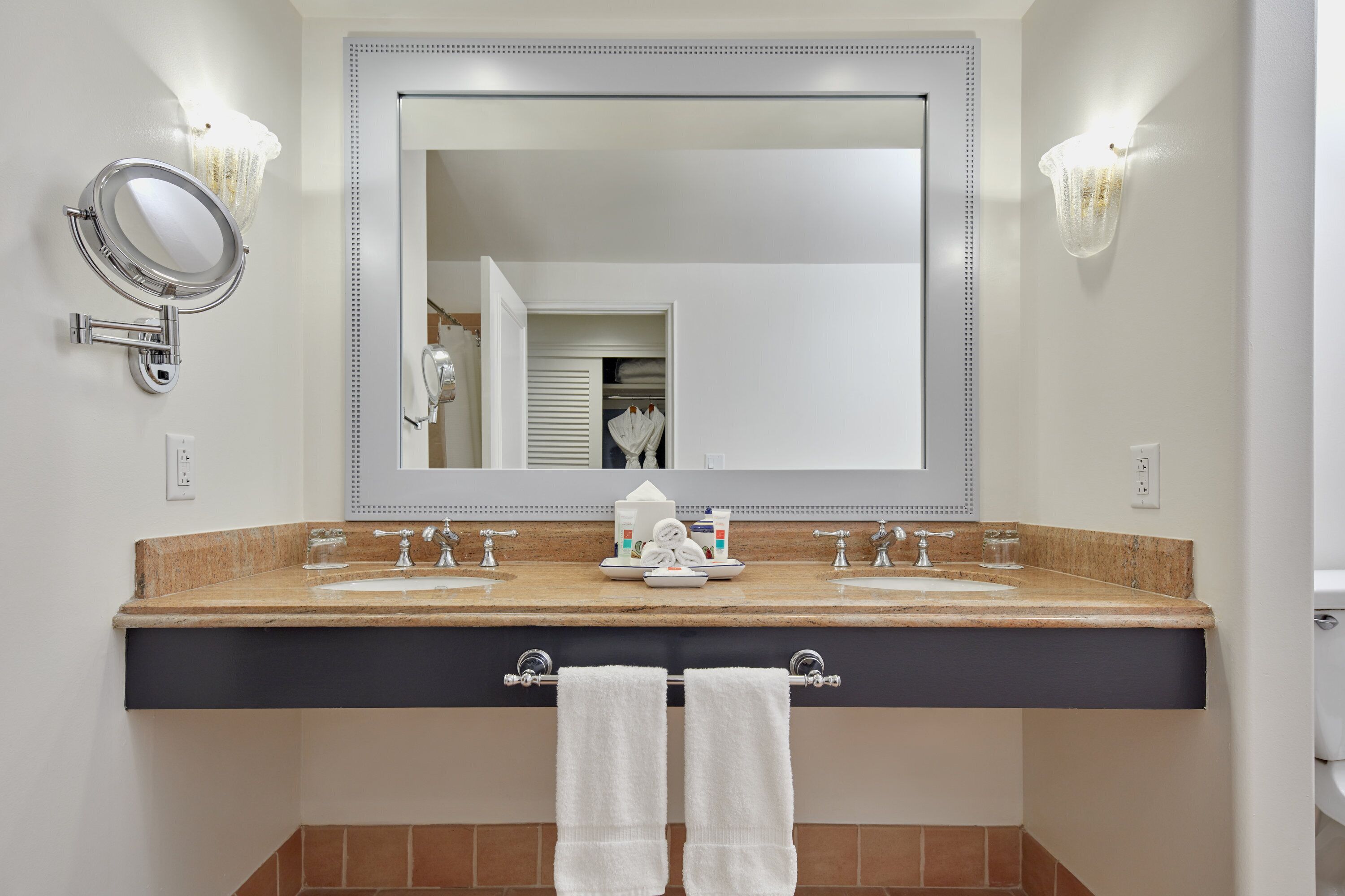Un baño con tocador de doble lavabo, un espejo grande y dos toallas colgadas en un perchero.