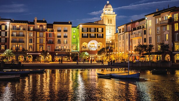 A waterfront promenade with colorful buildings, a prominent clock tower, and boats docked along the water. - Universal’s Loews Portofino Bay Hotel (Orlando)