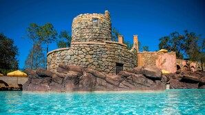 A stone castle-like structure with a circular tower, a pool in the foreground, and a clear blue sky. - Universal’s Loews Portofino Bay Hotel (Orlando)