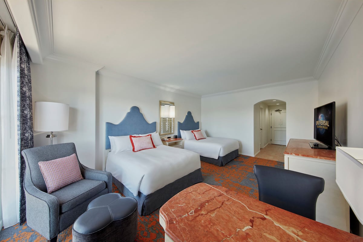 Ein Hotelzimmer mit zwei Betten, einem Schreibtisch, einem Stuhl, einer Couch und einem Fernseher.
