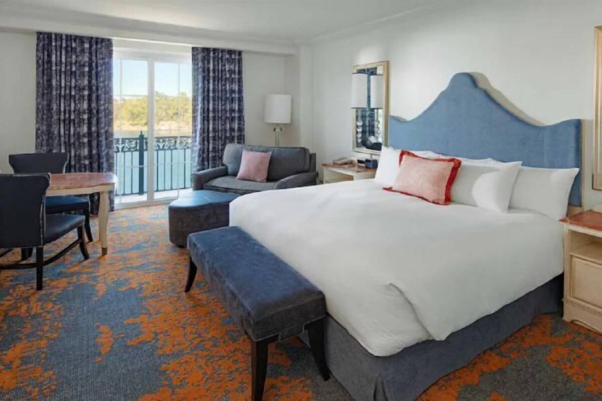 Une chambre d’hôtel avec un grand lit, un bureau, une chaise et un balcon avec des rideaux.
