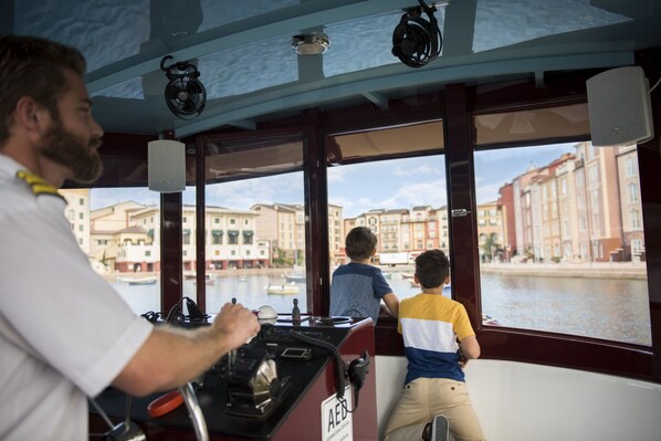 A boat interior with a steering wheel, control panel, and a view of buildings through the windows.