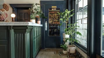Een smalle gang met een donkerblauwe deur die leidt naar een bar, met groene kasten en potplanten aan weerszijden.