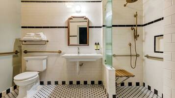 A bathroom with a toilet, sink, and shower area, including grab bars and a glass shower enclosure.