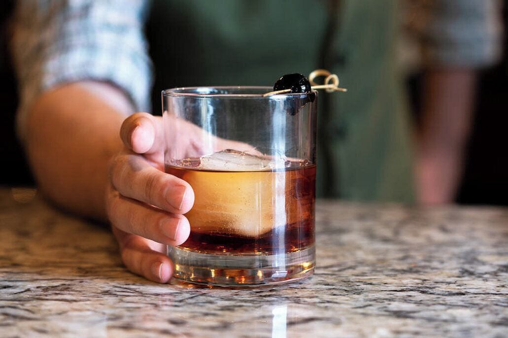 A person holding a glass with a layered drink and a garnish.