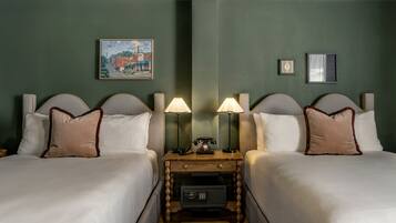 Habitación de hotel con dos camas, una mesita de noche con teléfono y caja fuerte, y obras de arte en las paredes.