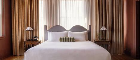 A large bed with a headboard, two bedside tables with lamps, and a window with curtains.