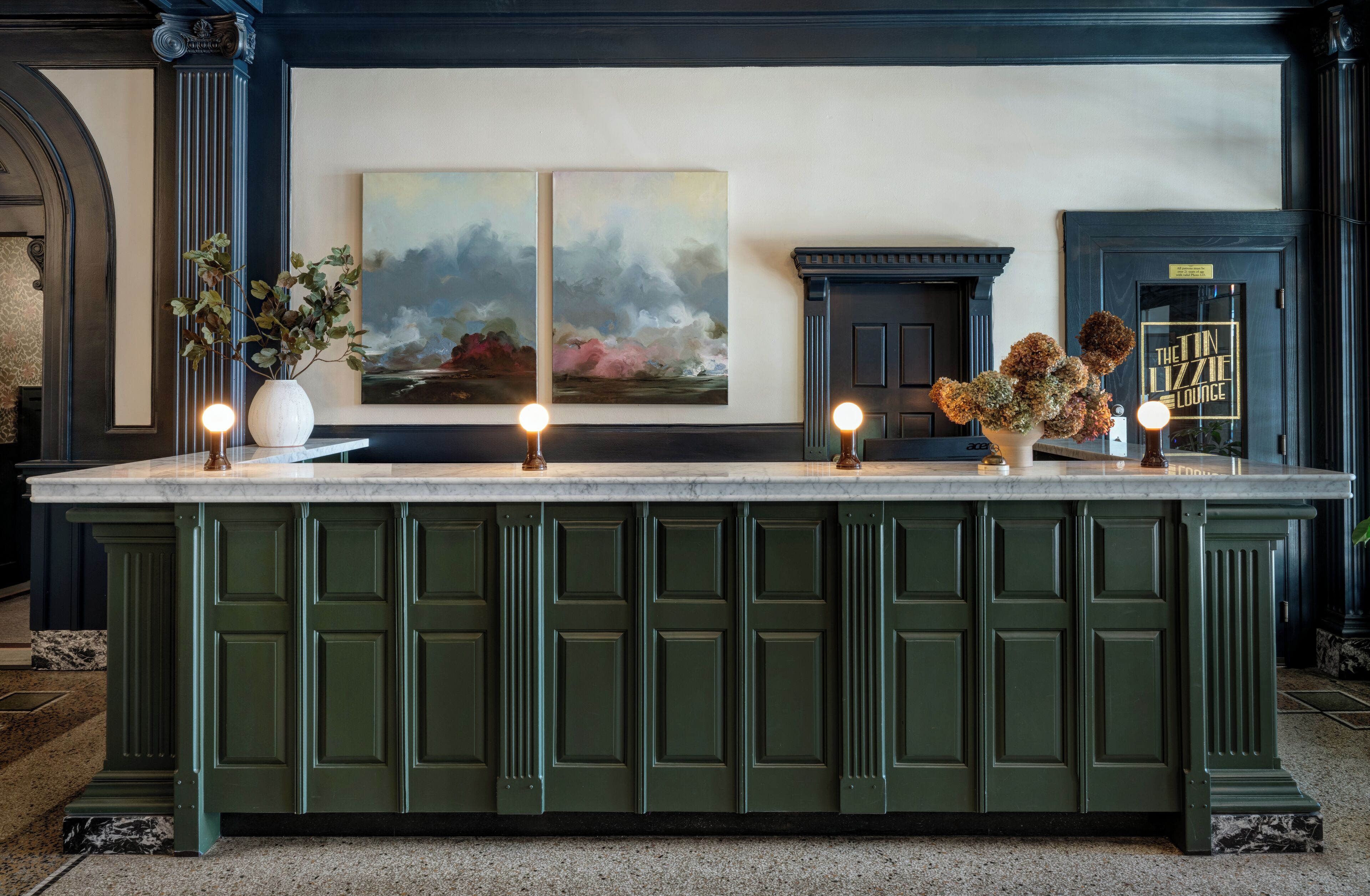 A bar area with a marble countertop, green cabinetry, and two paintings above.