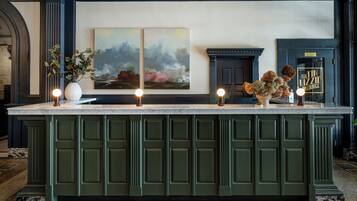A bar area with a marble countertop, green cabinetry, and two paintings above.