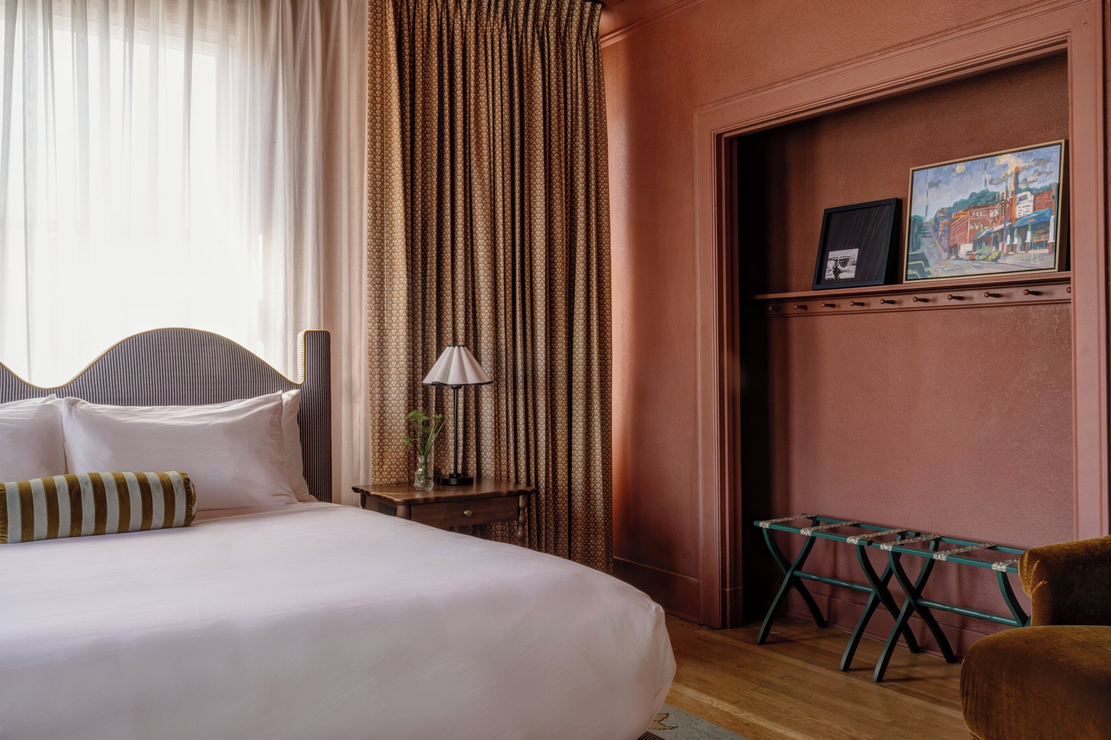A hotel room with a large bed, a small table with a lamp, a chair, and a painting on the wall.