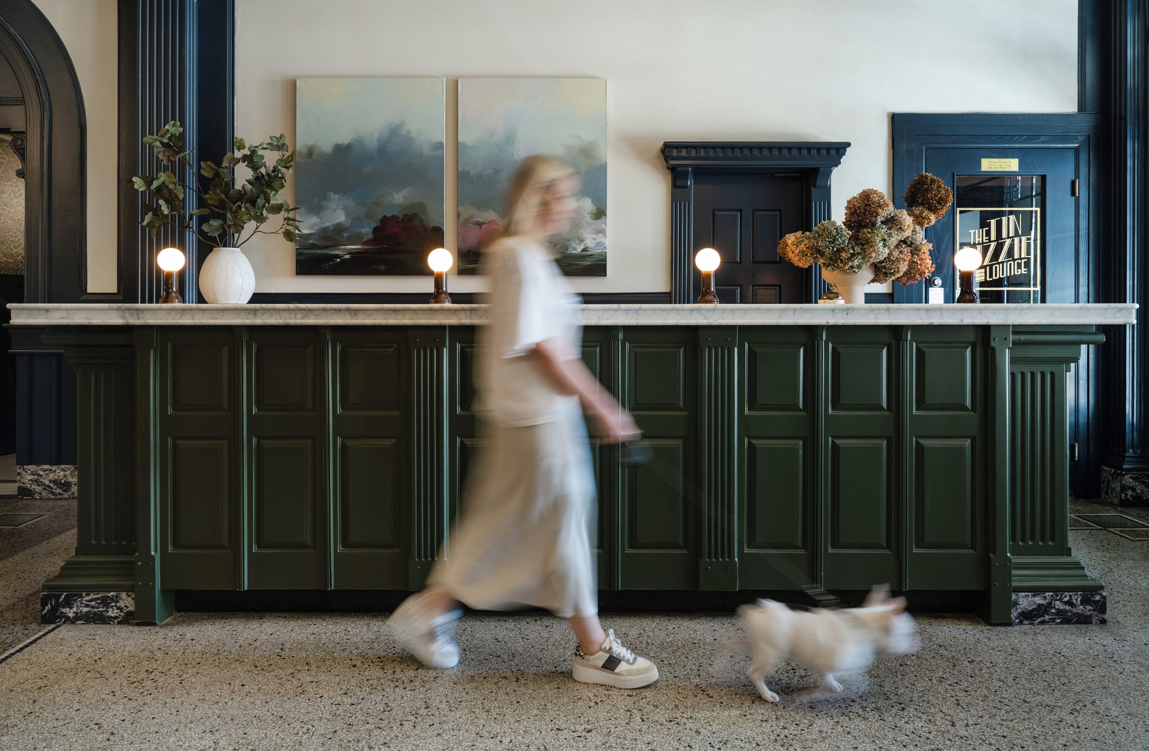 A lobby with a reception desk, green cabinets, a painting, and a sign reading "The Tin Lounge".