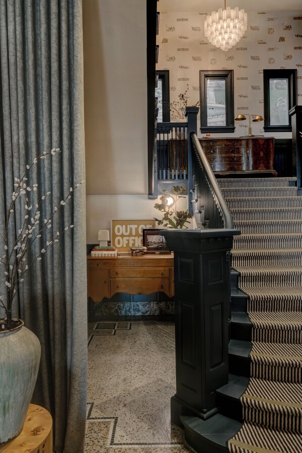 A staircase with a patterned carpet, a wooden desk with a sign, and a vase with branches.