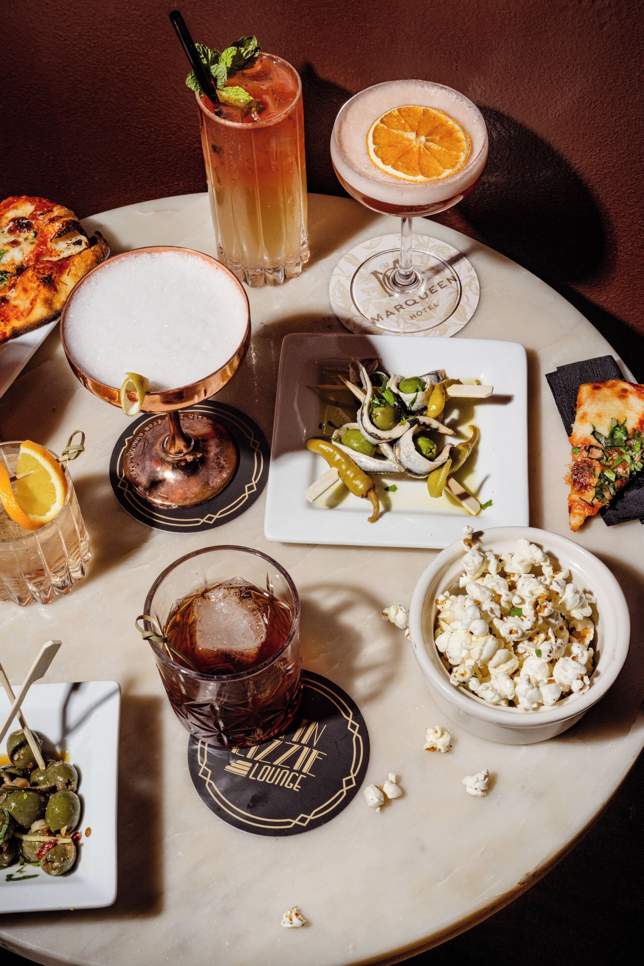 A table with various drinks, a pizza, and a bowl of popcorn.