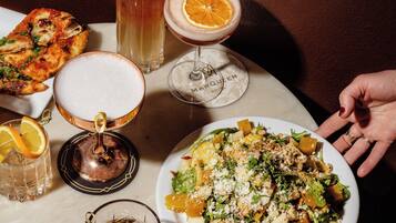 A table with various dishes and drinks, including a plate of salad, a glass of iced tea, and a cocktail.