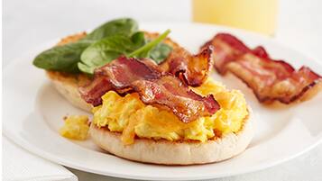 A breakfast plate with scrambled eggs, bacon, and spinach on a white plate.