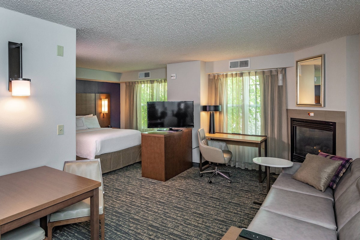A hotel room with a bed, desk, TV, and seating area.