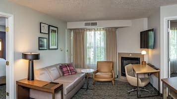 A hotel room with a bed, a sofa, a desk, a chair, a lamp, a fireplace, and a television.