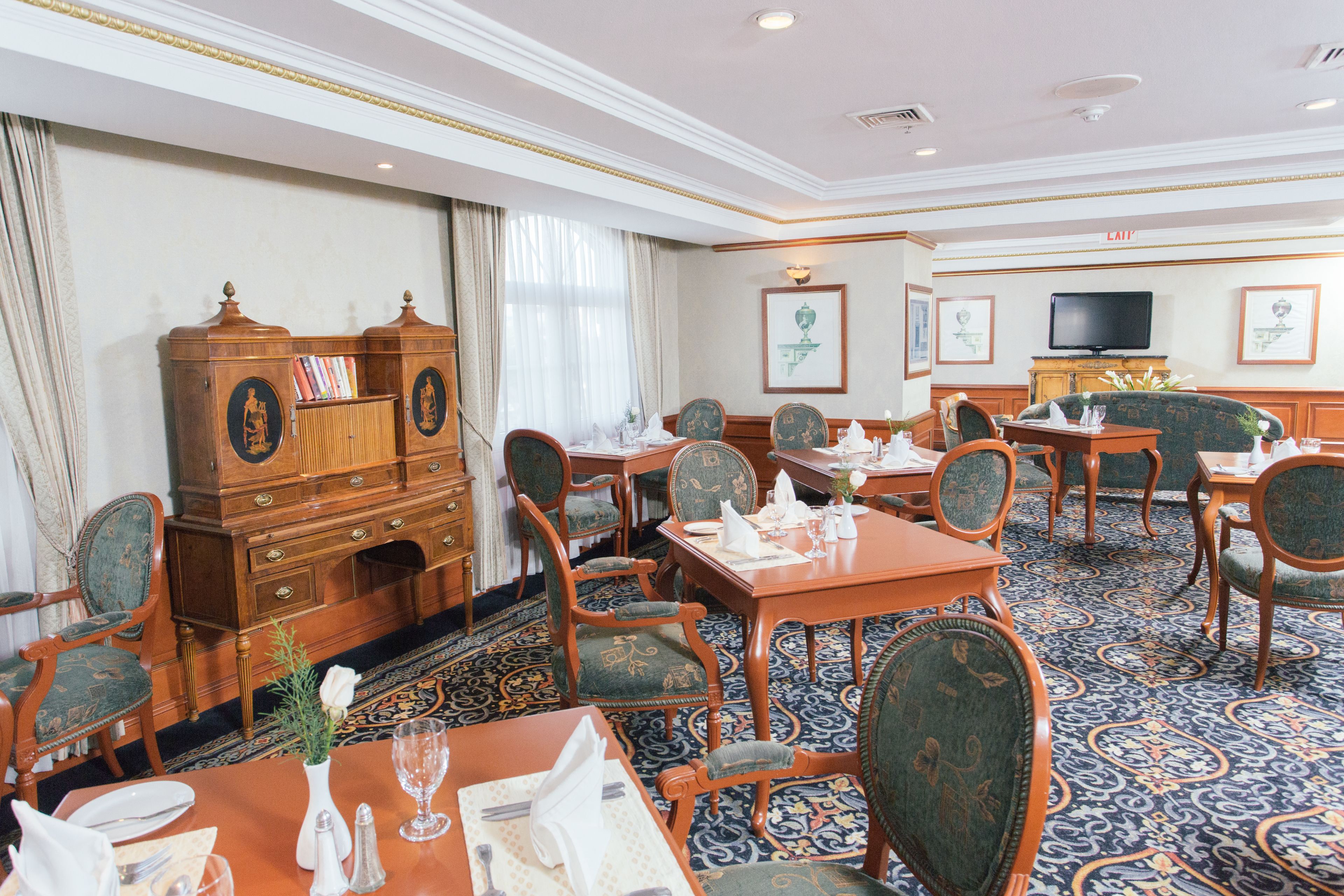 A hotel dining room with wooden furniture, a large cabinet, and a television on the wall.