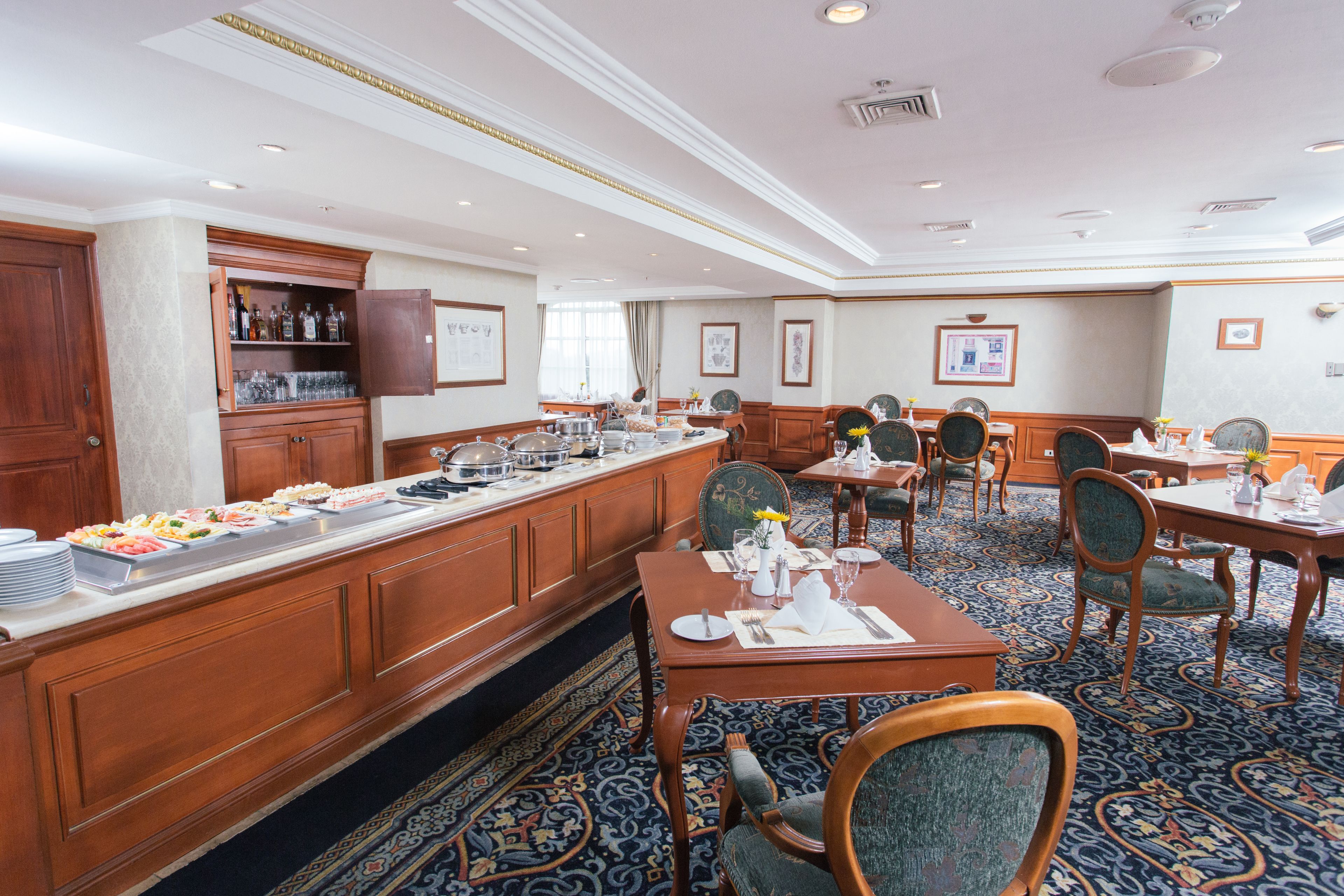 A hotel dining area with buffet service, multiple dining tables, and chairs.