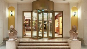 A revolving door entrance with marble steps leading up to it, flanked by two lion statues. - Hilton Princess Managua (Managua)