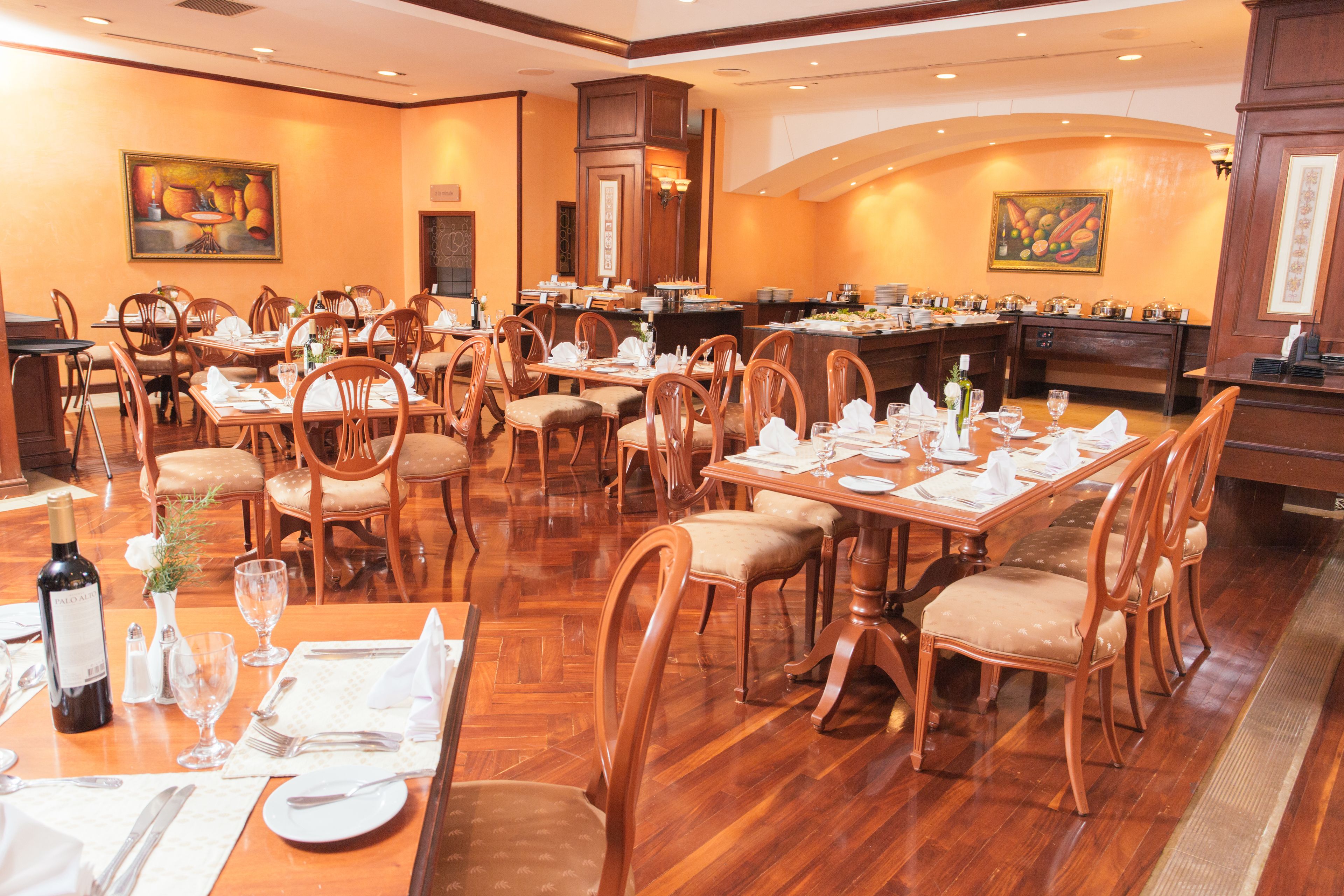 Un comedor amplio con mesas y sillas de madera, una barra central y obras de arte en las paredes.