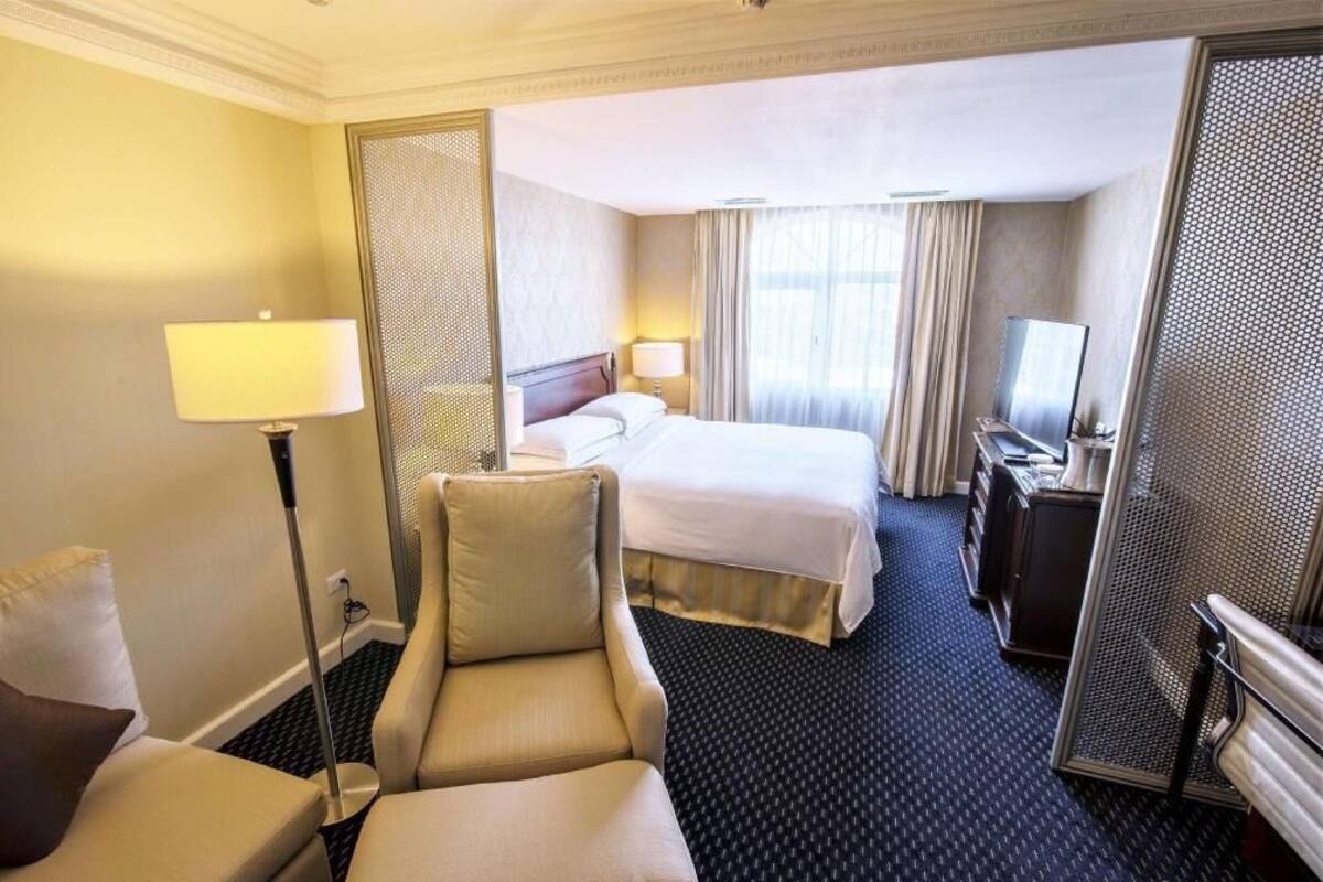 A hotel room with a bed, a desk, a chair, a lamp, and a television.